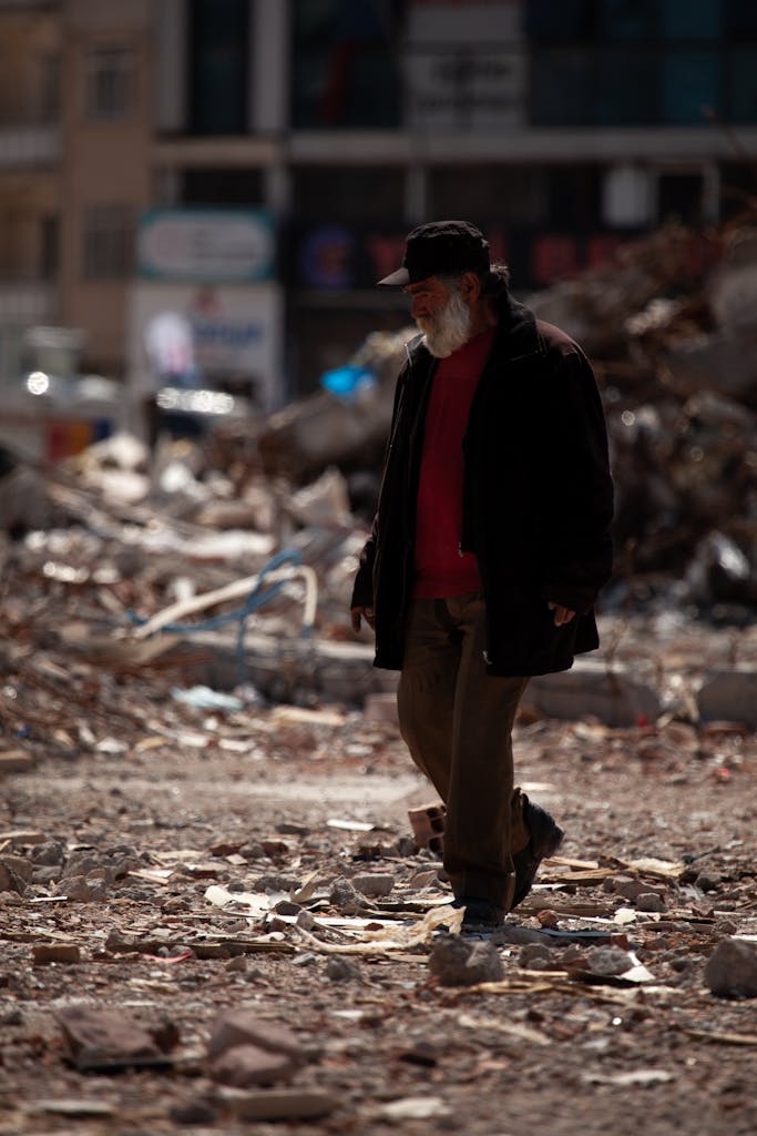 An elderly man walks alone through rubble in Malatya, Türkiye, post-earthquake scene.