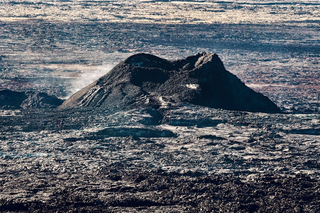 An expansive aerial view of a rugged lava field with a volcano at its center.