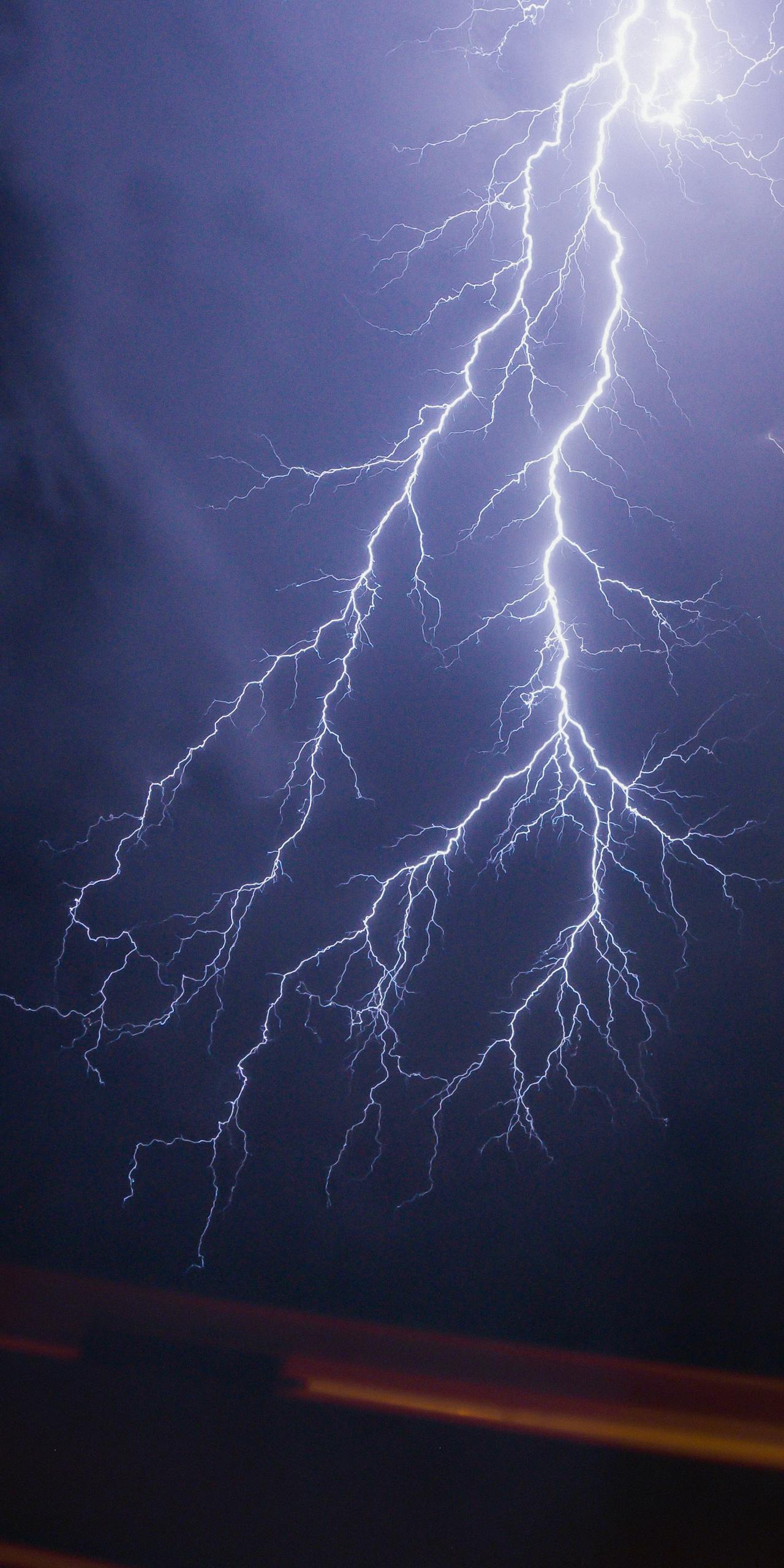 Intense lightning bolt illuminating a dark night sky during a powerful thunderstorm.