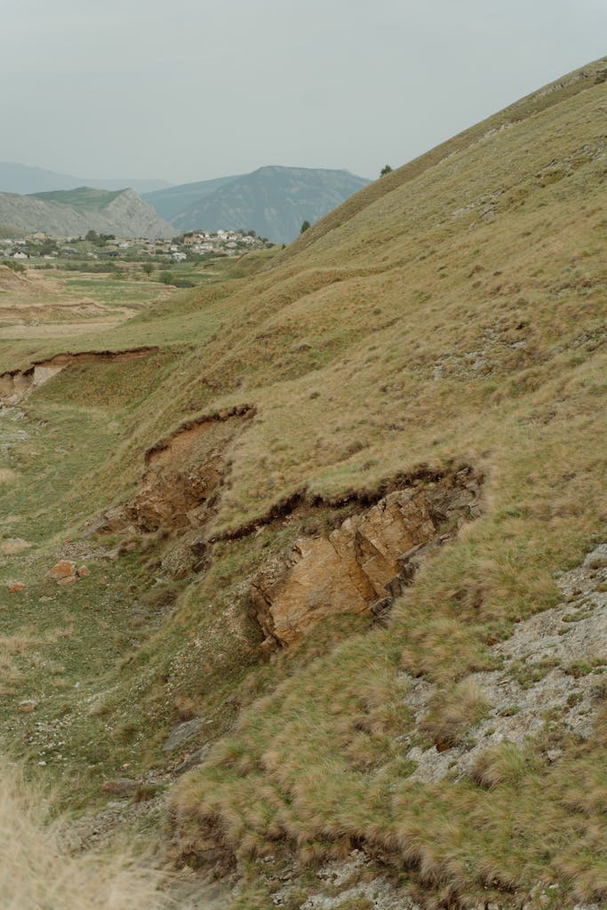 A detailed view of an eroded hillside with visible grass patches and soil layers in a rural landscape.