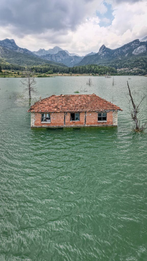 An abandoned house partially submerged in a serene lake surrounded by mountains in Serik, Antalya.